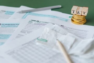 Stack of tax forms and coins with a 'TAX' stamp, symbolizing finance and accounting