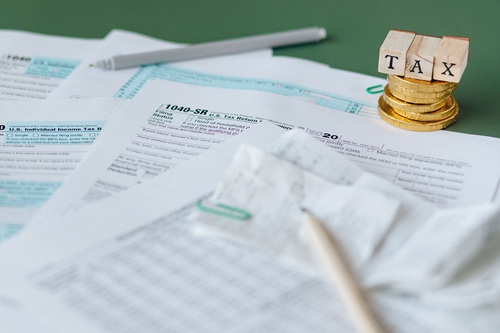 Stack of tax forms and coins with a 'TAX' stamp, symbolizing finance and accounting