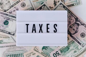US dollar bills with a white block spelling 'taxes'