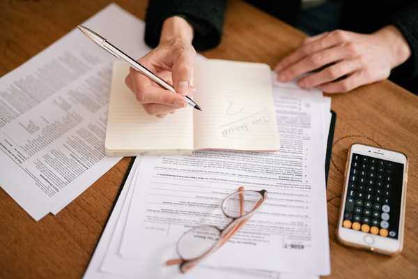 Close-up of a person writing in a notebook with documents and a calculator, managing finances